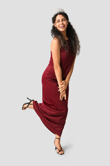 Beautiful young African-American woman in stylish red prom dress and tiara on grey background