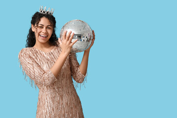 Beautiful young African-American woman in tiara and stylish dress with disco ball on blue background