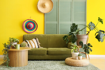 Interior of yellow living room with comfortable sofa, coffee table and houseplants