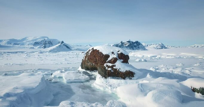 Winter Antarctic landscape in sunny day, blue sky. Desert white land of snow and ice, mountain range in background. Breathtaking travel journey over frozen Antarctica landscape. Low angle drone shot