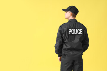 Teenage police officer on yellow background, back view
