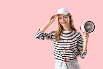 Young female lifeguard in cap with megaphone on pink background