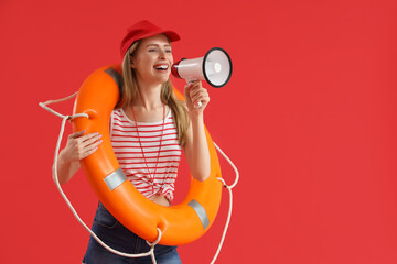 Young female lifeguard in cap with rescue ring and megaphone on red background
