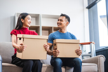 Young Asian couple relocating to a new house, joyfully packing and unpacking belongings. Expertise...