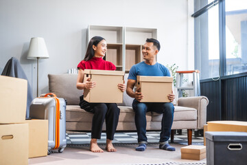 Young Asian couple relocating to a new house, joyfully packing and unpacking belongings. Expertise in moving, packing, togetherness, and creating a new home together.