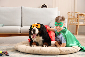 Boy and dog in superhero costumes lying on pet bed near sofa