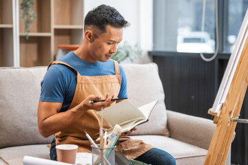 Fototapeta premium Middle-aged Asian man, skilled painting artist, donning an apron. Proficient in art, creativity, inspiration, and canvas work, utilizing various tools to express imagination.