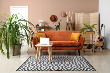 Interior of living room with houseplants, coffee table, laptop and soft sofa