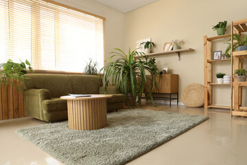 Beautiful interior of living room with houseplants, green sofa, shelving unit and coffee table