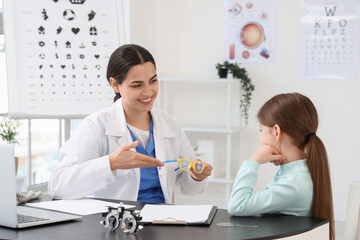 Female ophthalmologist giving little girl eyeglasses at table in clinic
