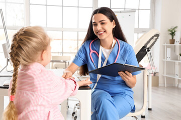 Female pediatrician working with little girl at table in clinic