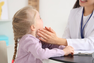 Female pediatrician examining little girl at table in clinic, closeup