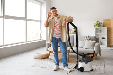 Young bearded man in headphones with vacuum cleaner at home