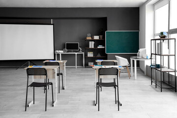 Interior of empty classroom with desks, projector screen and chalkboard