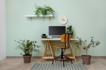 Modern workplace with computer monitor and houseplants near light green wall in office
