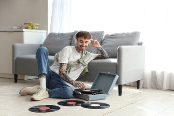 Young tattooed man with headphones and record player listening to music in kitchen