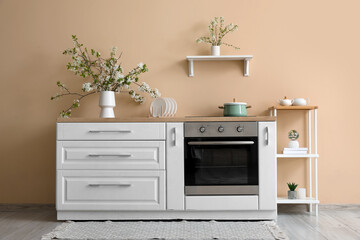 Vase with blooming branches on white counter in beige kitchen