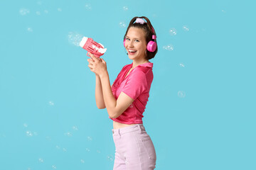 Happy teenage girl in headphones with soap bubble gun on blue background