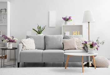 Interior of light living room with sofa and lilac flowers in vases