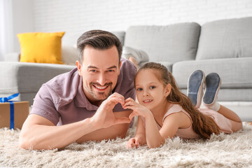 Father and his little daughter lying on floor and making heart with their hands in room. Father's Day celebration