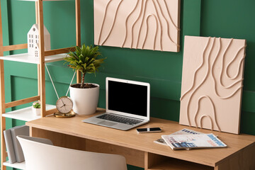 Interior of stylish room with workplace, laptop and picture on green wall
