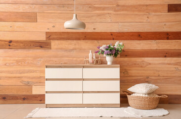 Stylish wooden cabinet, pillows and vase with flowers in room