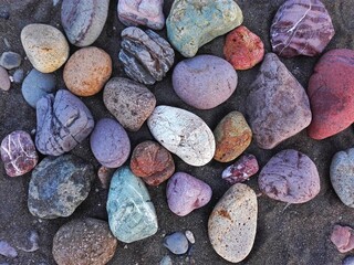 Pile colorful sea or lake pebble stones and rocks on beach. Different forms multicolor (green, orange, red, grey, black) as natural abstract pattern texture background. Close up river gravel on coast.
