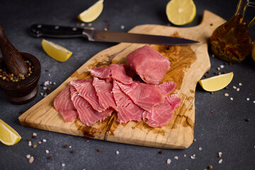 Woman cut tuna steak into slices on a wooden cutting board at domestic kitchen cooking tuna carpaccio