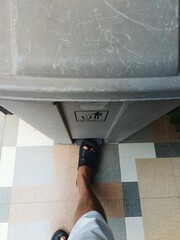 A man's foot steps on the pedal to open a trash can.