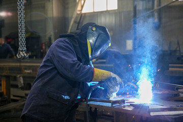 Skilled Welder in protection at Work with Sparks Flying in Industrial Workshop