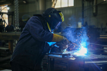 Skilled Welder in protection at Work with Sparks Flying in Industrial Workshop