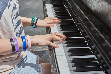 Black piano in a city square, with the hands of a musician playing. Close-up. Musical concept