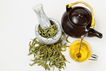 lemon verbena infusion in a glass cup with a marble mortar and pestle and a ceramic teapot with...