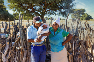 african village, family, mom , father and small baby, standing in front of the outdoors kitchen in...