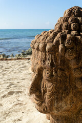 Close-up of the face of the Buddha statue at a tropical beach facing the sea, palm trees and hammocks in the background 