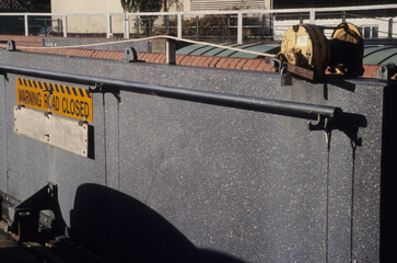horizontal image of a solid metal walled barrier. Warning Road Closed sign on panel. Iron work pulley system. Padlock attached. closeup. Location Woodbridge Railway station Suffolk UK 2003