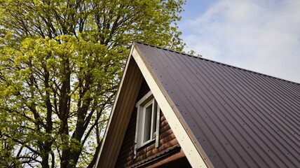 Brown metallic roof of house under the spring tree against blue sky