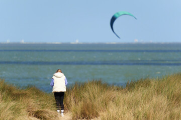 Kiteboarding in Holland. Water sports in summer in sunny weather. Woman on the dune, rear view....