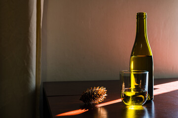White glass and opened green bottle of wine with cork and pine cone on table in sun ray. Classic winery cellar beautiful image