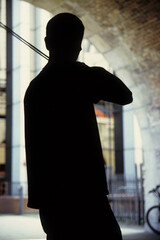 vertical image of a man playing his violin. busking under a stone arch. back view silhouette only visible. Location Thames Bank London UK 2003