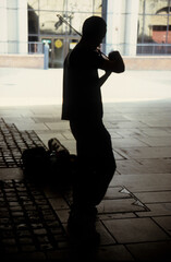 vertical image of a man playing his violin. busking under a stone arch. side view silhouette only...