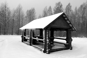 Wooden pavillion in snow with icicles on roof. Black and white