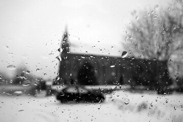 View on winter church and car through wet windshield with rain drops. Black and white