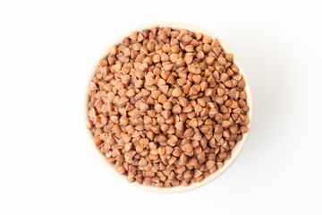 Uncooked, brown buckwheat grains in bowl on white background. Dry buckwheat grains. Top view