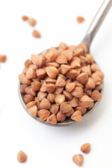 Dry, brown buckwheat grains in iron spoon on white background. Close-up