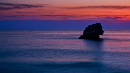 Fototapeta na wymiar A stone in a calm sea at sunset. Creative, AI Generated