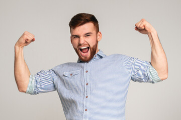 Young muscular man showing his power in biceps on camera at beige background, panorama, copy space
