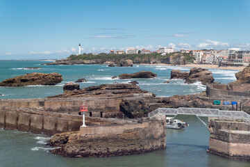 Tranquilidade costeira: Rochas marítimas em Biarritz sob o Sol com um contorno urbano no horizonte