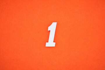 The number 1 is made from white painted wood placed on a background of orange paper.