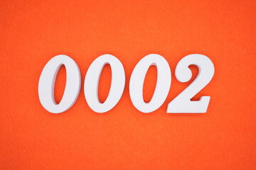 The number 0002 is made from white painted wood placed on a background of orange paper.